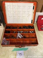 Full open orange metal compartment case showing multiple compartments stocked with automotive drain plugs and washers. White printed spec sheet inside lid.