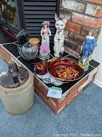 Overview of decorative figurines, ceramic jug, plates, and incense holder on brick surface