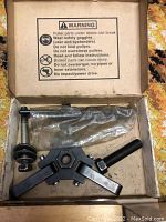 Harmonic damper pulley puller tool inside a box with warning label on the inner lid, black metal body with threaded components.