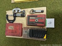 Photo showing double flaring tool in red case, micrometer, pipe cutter, plastic organizer with clips and fasteners, and steering wheel remover.