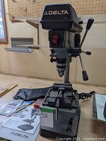 Full view of Delta benchtop drill press on workbench showing head, column, table and base