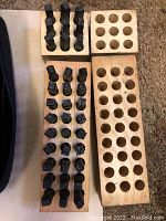 Letter and number die cast stamps arranged in wooden holders with holes. Various characters visible.