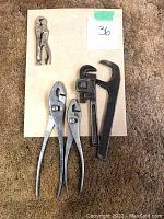 Photo showing one pipe wrench, three pliers, and one pair of vice grips on a beige board with lot number 36.