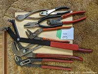 Photo of six assorted pliers and cutters arranged on a beige surface showing variety of sizes and handle colors.