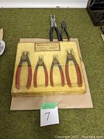 Four retaining ring pliers with red handles in original yellow Snap-on packaging laid flat on green surface.