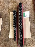 Top view of two red metal socket holders with a range of sockets arranged from smallest to largest.