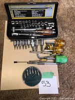 Socket set open with many chrome sockets and handles. Multiple screwdrivers with yellow and green handles and assorted bits
