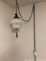 Full view of the hanging light fixture showing the textured bulbous glass shade, black metal suspension, and chain.
