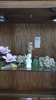 Porcelain angel and flower figurines displayed in wooden cabinet.