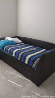 Front angled view of brown twin size daybed with two pillows and striped blanket, shows padded headboard and footboard.