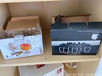 Two boxes on a shelf: left is Circle Fancy 4-piece dessert parfait cups, right is City Chic 5-piece shot glass set box.