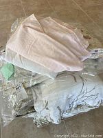 Stack of bedding including light pink and taupe floral quilt, wrapped in packaging with saw tag showing
