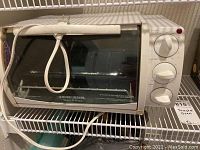 Photo of the Black & Decker white toaster oven showing the front glass door with white handle and three control knobs on the right side.