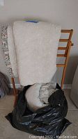 Wooden blanket rack with quilts draped over it and quilts rolled in black bag below