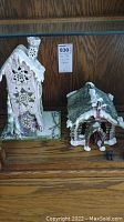 Two Blue Sky porcelain candle houses on a wooden shelf, including a tall house with star cutouts and a smaller green house with snow accents and candy cane pillars.