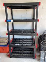 Front view of the full black plastic shelving unit with four shelves and red corner accents.