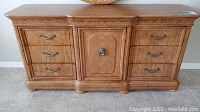 Front view of wooden Wynwood 9 drawer dresser with curved drawer fronts and central cabinet door, showing warm finish and metal handles.