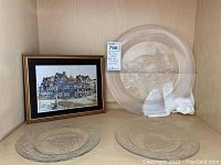Framed Chester Cross art propped beside three clear glass serving bowls of varying sizes on a wooden shelf.