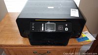 Front view of the black Kodak ESP 7 printer placed on a wooden surface with visible stickers.