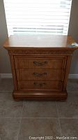 Front view of the wood nightstand showing three drawers and carved detail on top edge.
