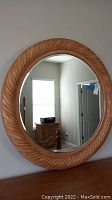 Full front view of round mirror showing beveled glass and carved wooden frame with leaf or feather pattern.