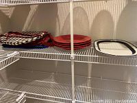 Red and white serving plates stacked alongside cloth placemats on a wire shelf