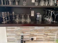 Shelf with multiple types of clear glass stemware including wine glasses and short glasses, some with chips on rims.