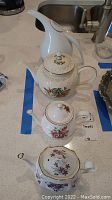 Four assorted porcelain/ceramic teapots showing different floral designs and shapes on a kitchen counter.
