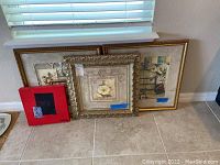 Four framed wall art prints resting on floor near window showing varied sizes and frame styles