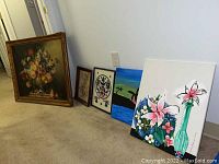 Wide shot showing all five paintings leaning against the wall, showing size variation and diverse subjects.