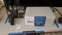 Brinks fireproof security box with blue lock and keys on table alongside Panasonic phone system