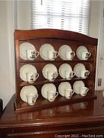 Wide shot of full display shelf featuring 12 Hummel miniature teacups with matching saucers arranged on three tiers.