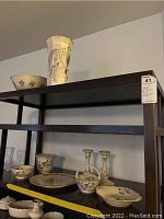 View of dark wood shelves displaying the vase, serving bowls, plate, candlesticks, and small decorative items arranged with visible floral pattern details