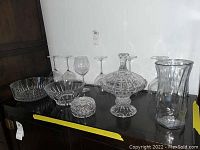 Wide view of all Lenox crystal items including glasses, bowls, candy dish, vase, and covered dish on a dark surface.