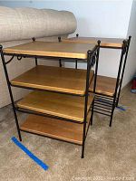Overall view of two shelving units showing four wood shelves each within black metal frames with decorative scrollwork and finials.