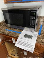 View of Panasonic microwave with control panel and manual on countertop, showing overall size and condition.