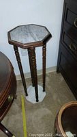 Full view of wooden plant stand with marble top and bottom showing turned legs.