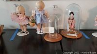 Two Danbury Mint porcelain dolls on stands, one in a pink dress about 12 inches and one with a blue dress about 11 inches. Two glass domes with wooden bases, one housing an antique Japanese doll.
