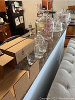 Countertop displays two boxed items and several clear glass cake plates with dome covers alongside a set of twelve clear glasses.