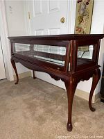 Full view of the wooden sofa table with glass panels and curved legs adjacent to a door.