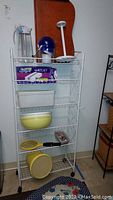 Front view of white metal storage shelf with multiple kitchen-related items on shelves.