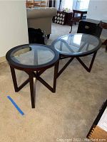 Photo showing both oval coffee table and round side table with glass tops and wooden frames in a living room setting.