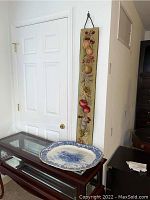 Full view showing vintage blue and white ceramic wall platter on the glass table and tall vertical fruit-themed textile wall art hanging on the wall.