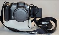 Front view of Canon Powershot S3IS digital camera with lens cap on lens, LCD screen flipped out, and attached Canon strap.