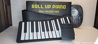 Roll up piano keyboard arranged with the pedal on a table with packaging in the background.
