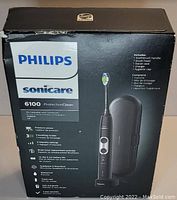 Box packaging of Philips Sonicare 6100 ProtectiveClean electric toothbrush showing product image and list of included items and features.