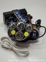 Black rechargeable headlamp with multiple LED bulbs and adjustable strap, with USB charging cable shown in front.