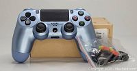 Titanium blue Sony PlayStation 4 wireless controller in front of a plain cardboard box. Accessories in plastic packaging are visible next to controller.