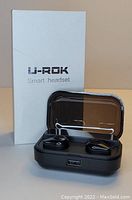 Black U-ROK wireless earbuds in their charging case alongside the white product box.