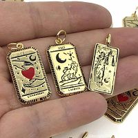 Close-up of three tarot card pendants held in hand showing intricate designs and gold plating.
